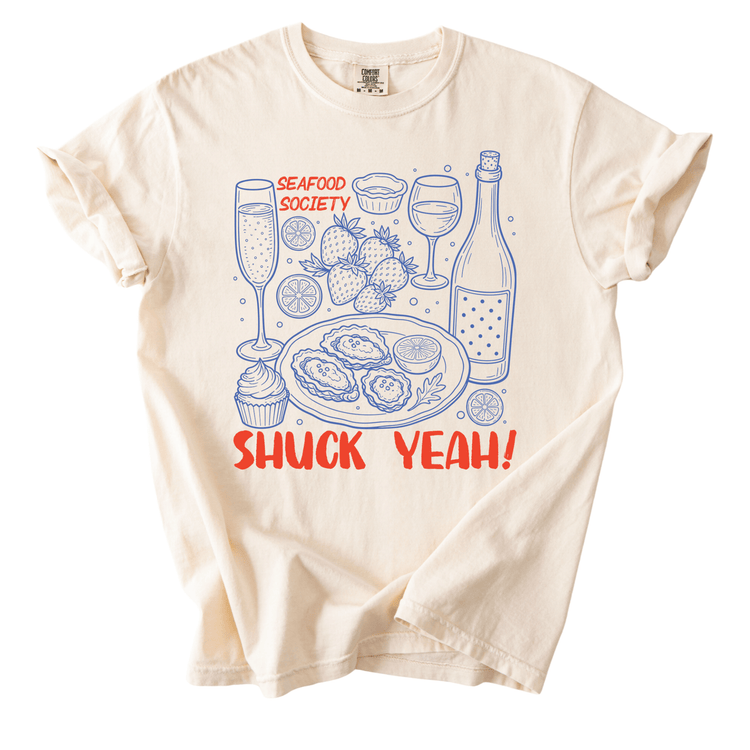 a t-shirt with a graphic design depicting various seafood items, including oysters, shrimp, and a bottle of wine, along with the text "SHUCK YEAH!"