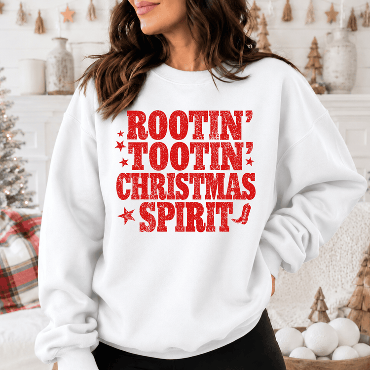 A woman wearing a white sweatshirt with a red text design that says "ROOTIN' TOOIN' CHRISTMAS SPIRIT".