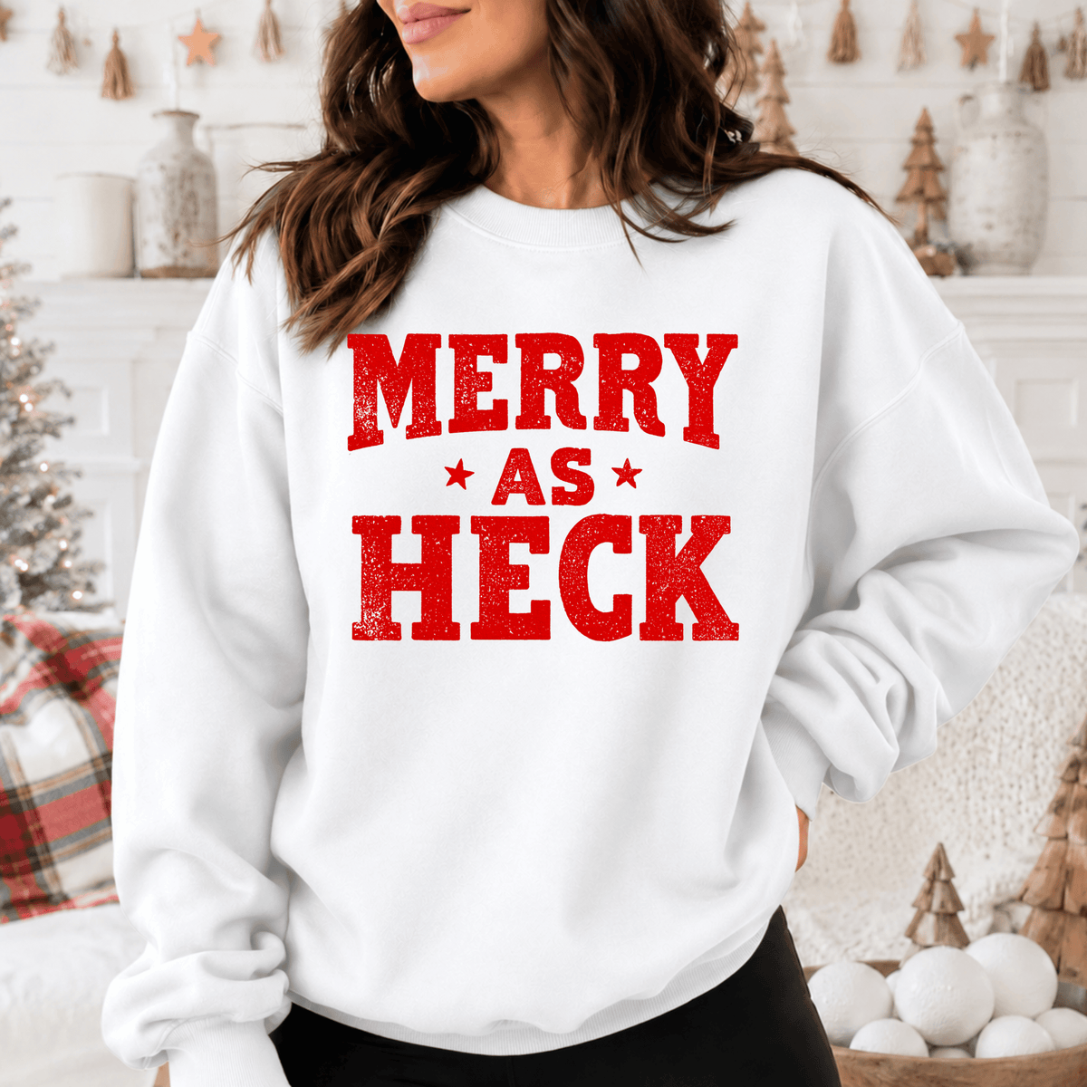 A woman wearing a white sweatshirt with the text "MERRY AS HECK" printed on it.