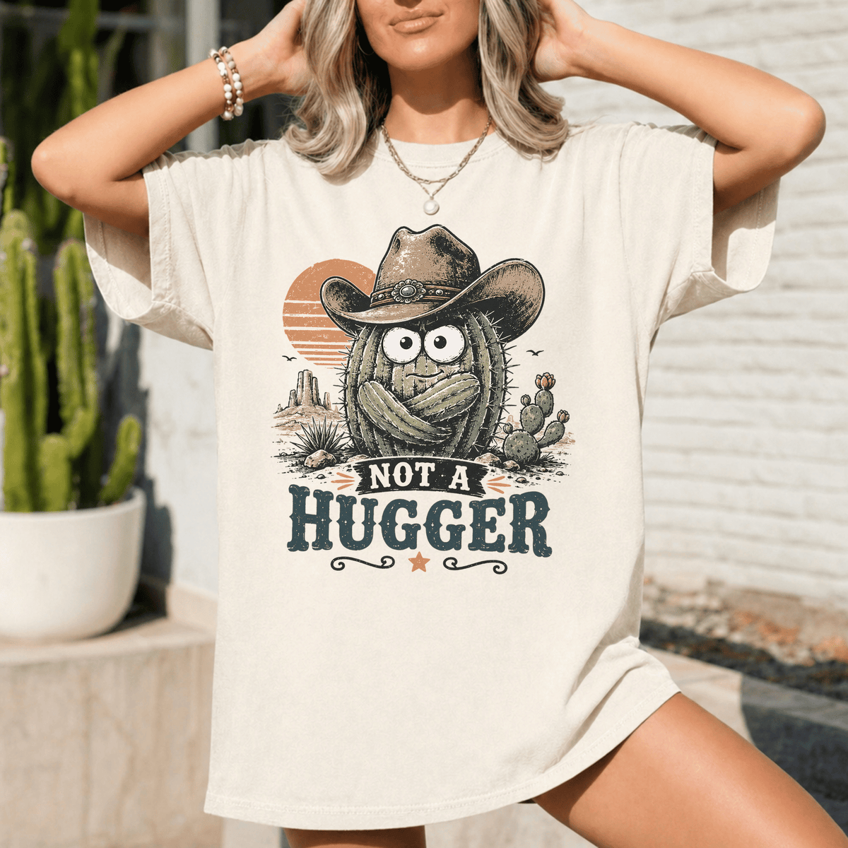 A woman wearing a white t-shirt with a graphic design of a cactus wearing a cowboy hat and the text "NOT A HUGGER" printed on it.