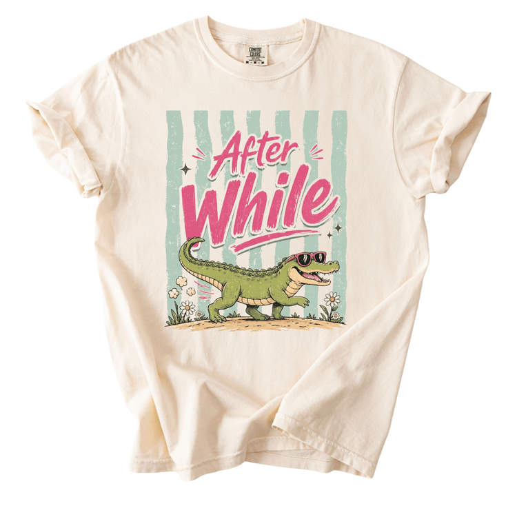 A white t-shirt with a graphic design featuring a green alligator wearing sunglasses and the text "After While" written above it.