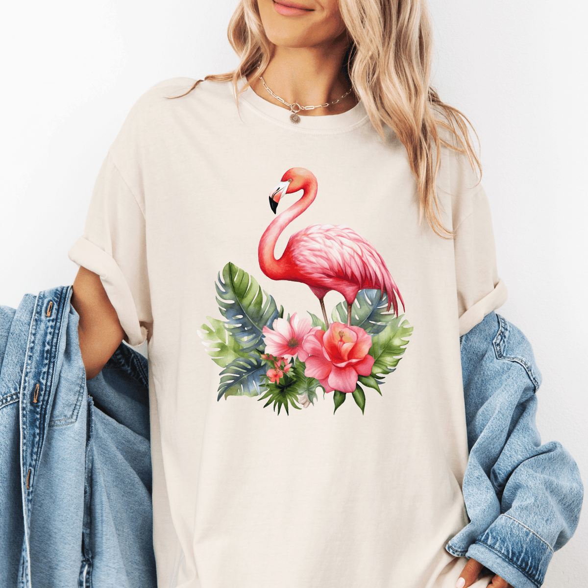 A woman wearing a white t-shirt with a pink flamingo and tropical flowers printed on it, standing against a white background.