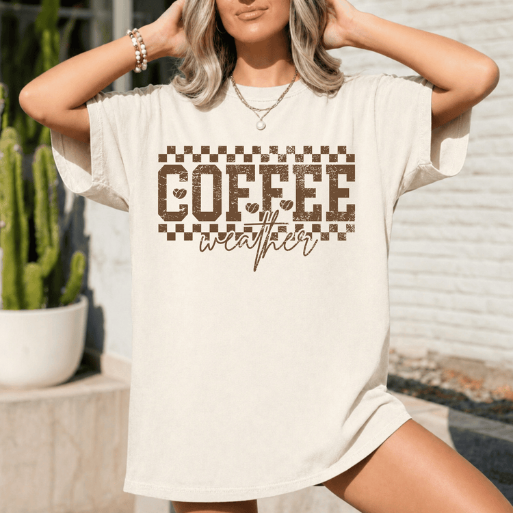 A woman wearing a white t-shirt with the text "COFFEE weather" printed on it, posing with her hands on her head.