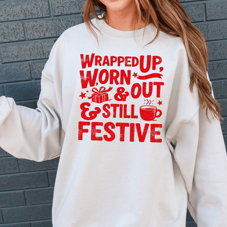 A white sweatshirt with a red graphic design that reads "WRAPPED UP, WORN OUT & STILL FESTIVE" along with various icons and text.