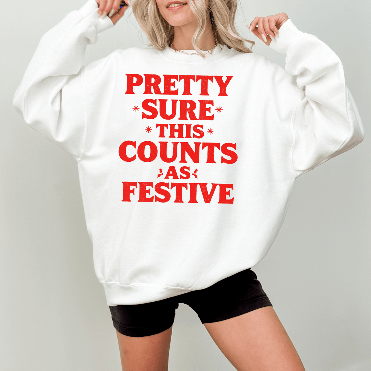 A woman wearing a white sweatshirt with red text that says "PRETTY SURE THIS COUNTS AS FESTIVE".