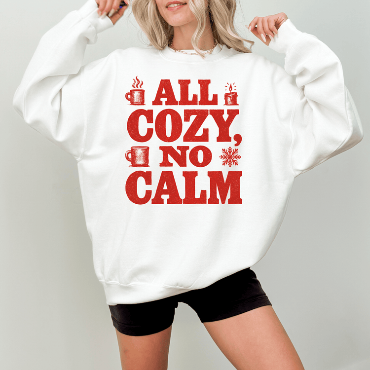 A woman wearing a white sweatshirt with the text "ALL COZY, NO CALM" printed on it.