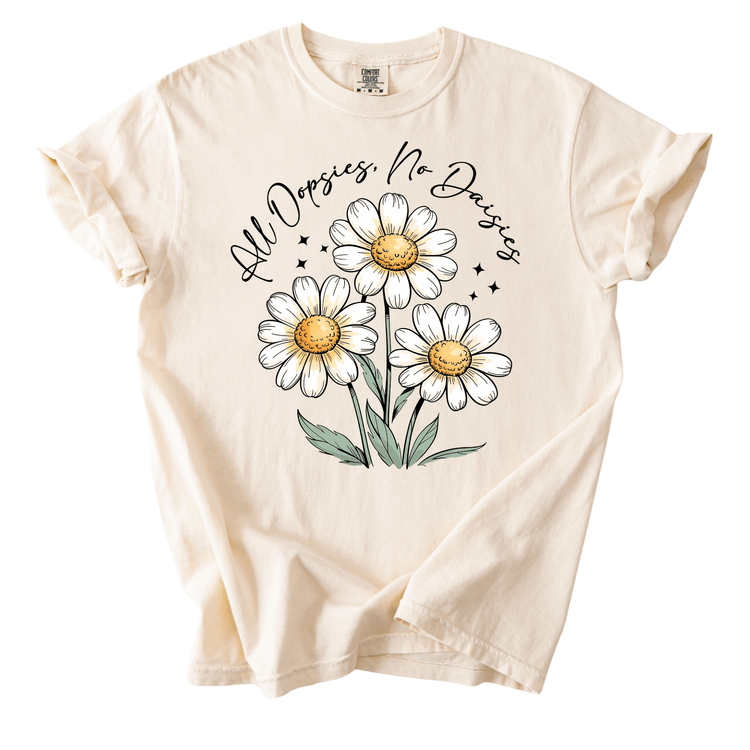 A white t-shirt with a graphic design featuring three white daisies with yellow centers and green leaves. The text above the daisies reads "All Dopsies No Dopsies".