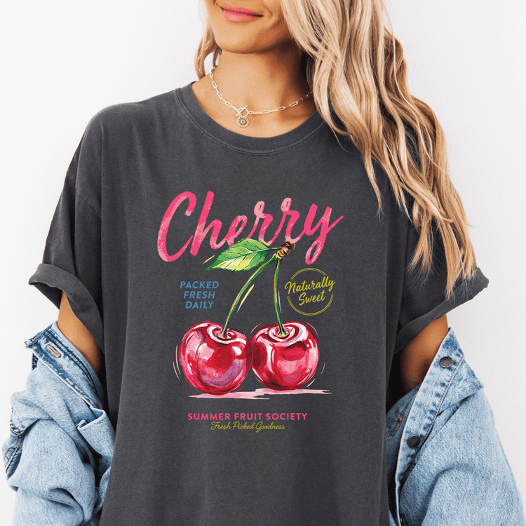 A woman wearing a gray t-shirt with a graphic design of cherries and text promoting a summer fruit society.