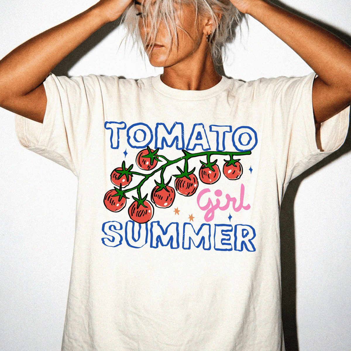 A person wearing a white t-shirt with a graphic design featuring a tomato and the text "TOMATO GIRL SUMMER".