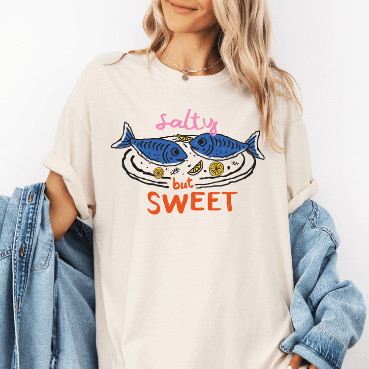 A woman wearing a white t-shirt with a graphic design of two fish and the text "Salty but Sweet" printed on it.
