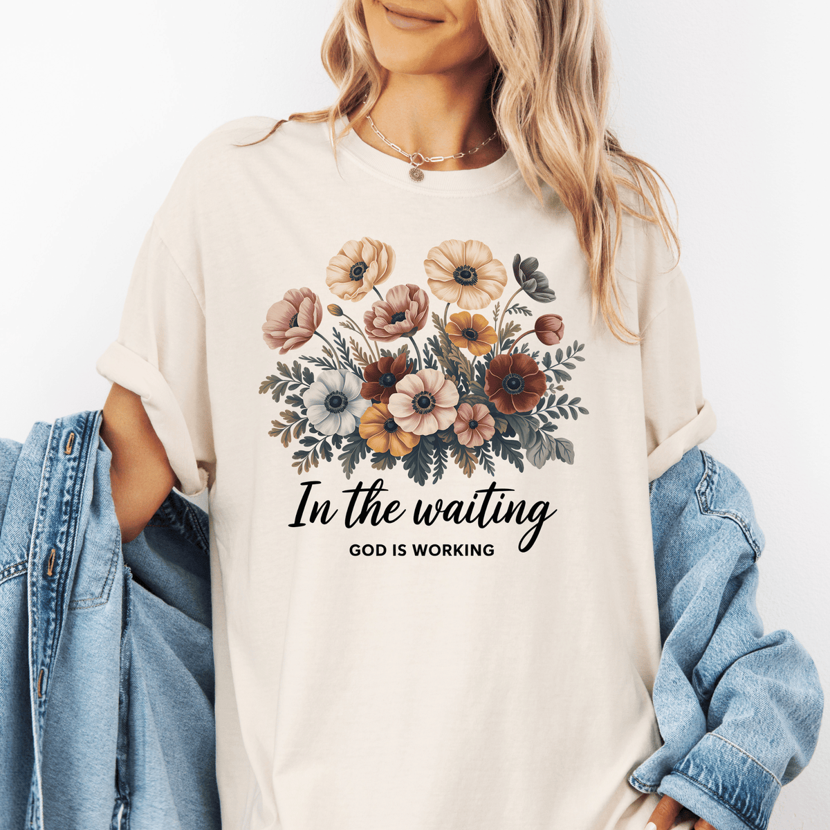 A woman wearing a white t-shirt with a floral design and the text "In the waiting God is working" printed on it.