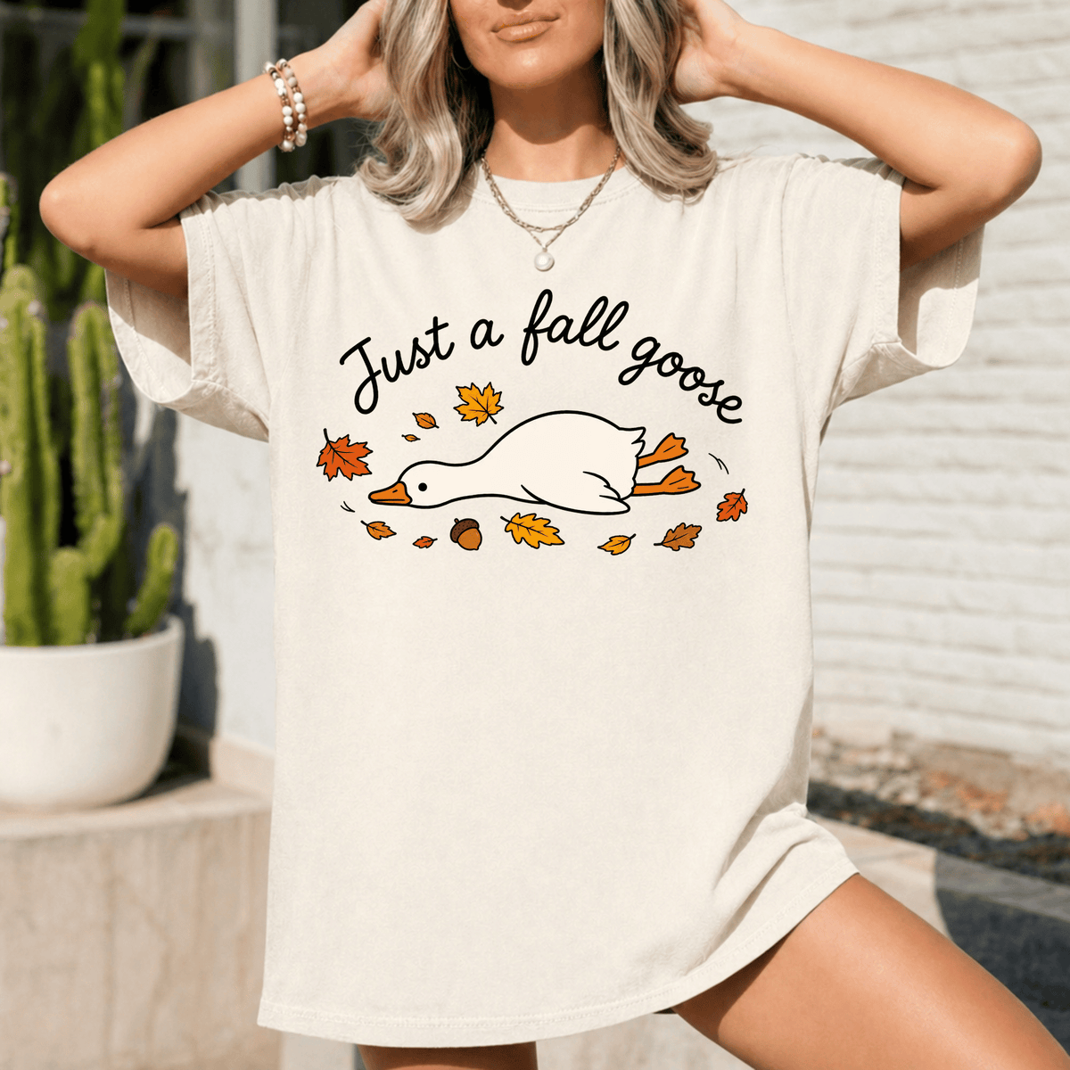 A woman wearing a white t-shirt with a graphic design of a goose surrounded by autumn leaves.