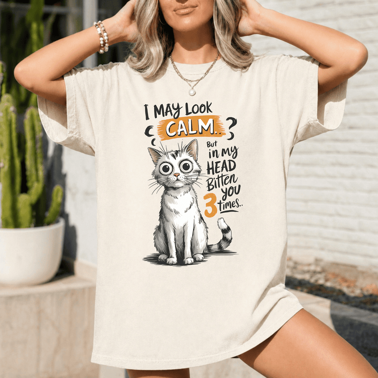A woman wearing a white t-shirt with a graphic of a cat and text that says "I may look calm, but my head bitten 3 times".
