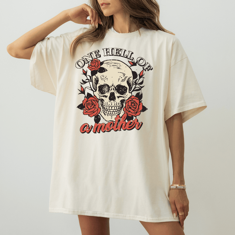A woman wearing a white t-shirt with a graphic design of a skull and roses, along with the text "One Hell of a Mother".