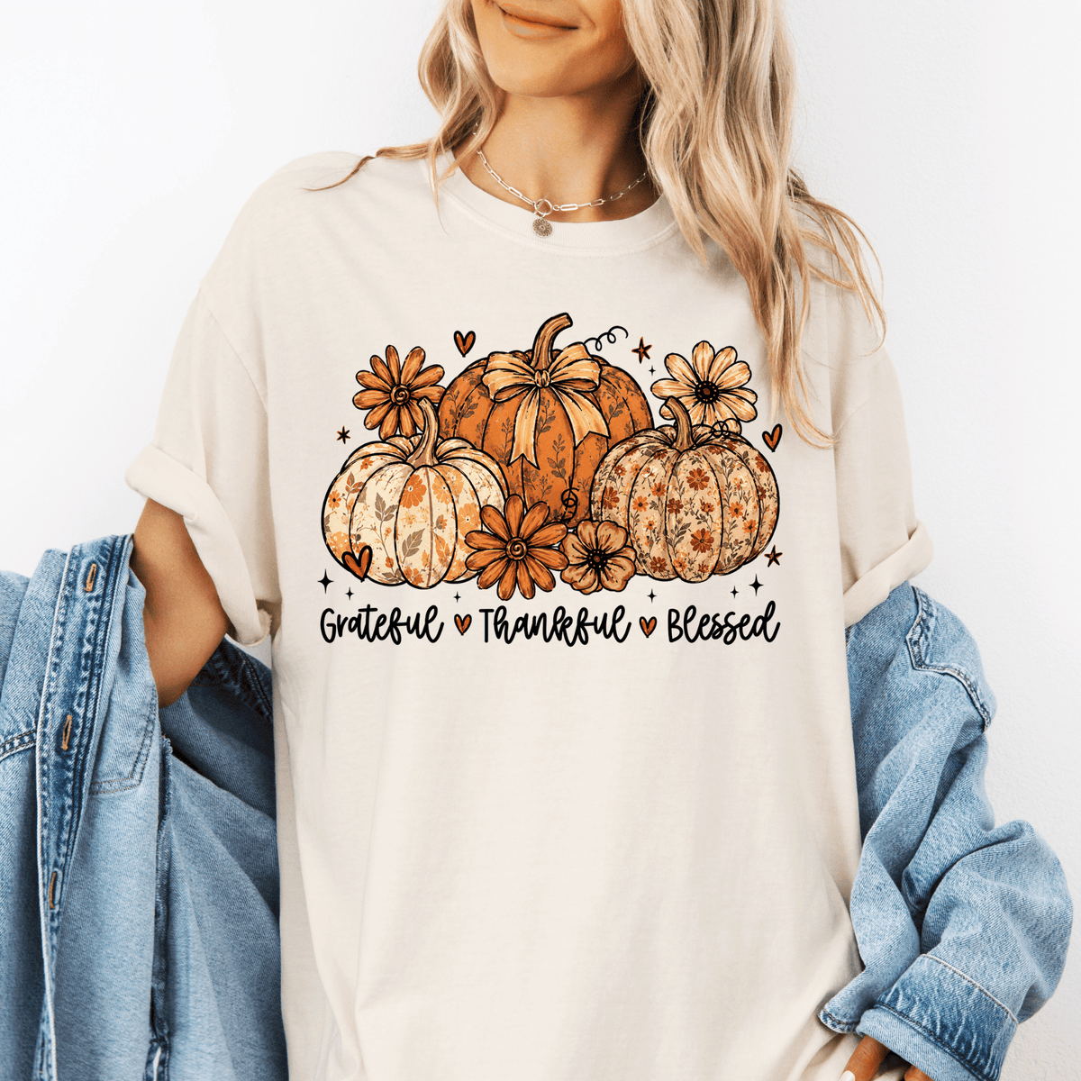 A woman wearing a white t-shirt with a graphic design of pumpkins and flowers, along with the text "Grateful, Thankful, Blessed".
