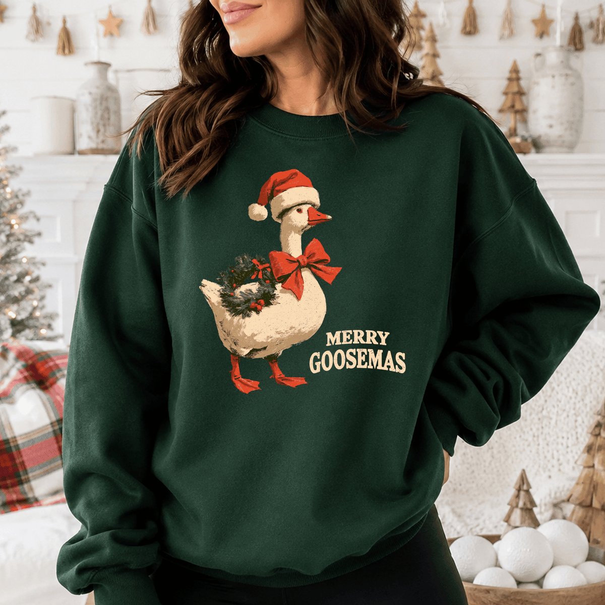 A woman wearing a green sweatshirt with a graphic of a goose wearing a Santa hat and holding a Christmas wreath.
