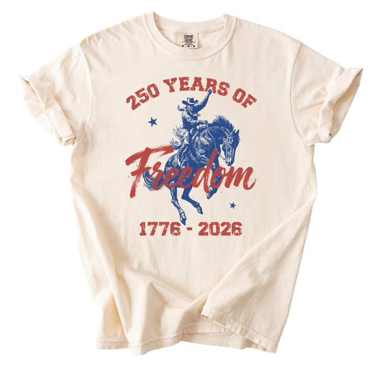 A white t-shirt with a graphic design featuring a cowboy on a horse and the text "250 YEARS OF Freedom" and "1776-2026".