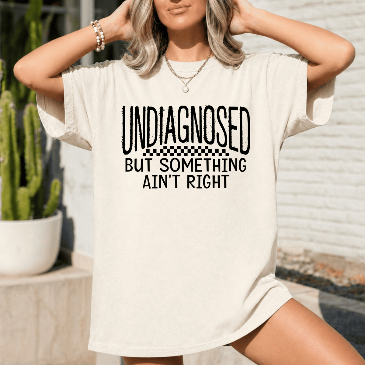 A woman wearing a white t-shirt with the text "UNDIAGNOSED BUT SOMETHING AIN'T RIGHT" printed on it.