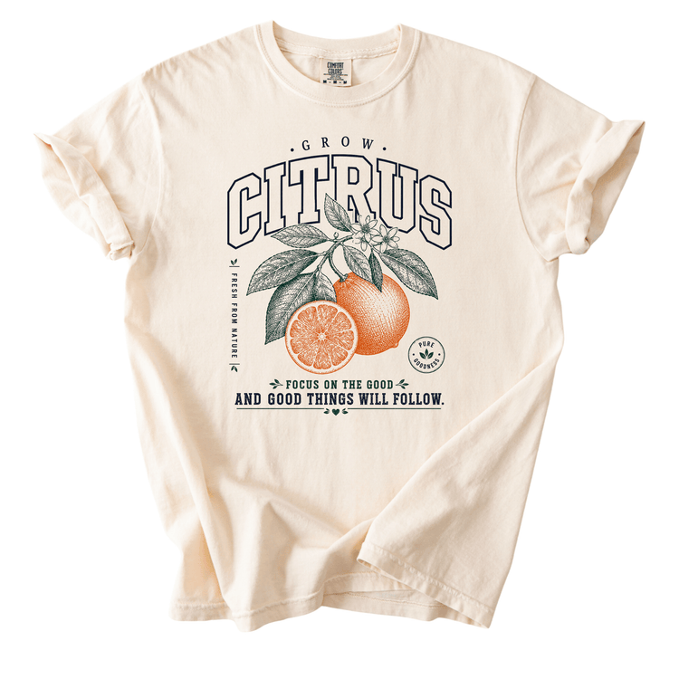 A white t-shirt with a graphic design featuring an orange and a leaf, along with text that reads "GROW CITRUS" and "Focus on the good things will follow".