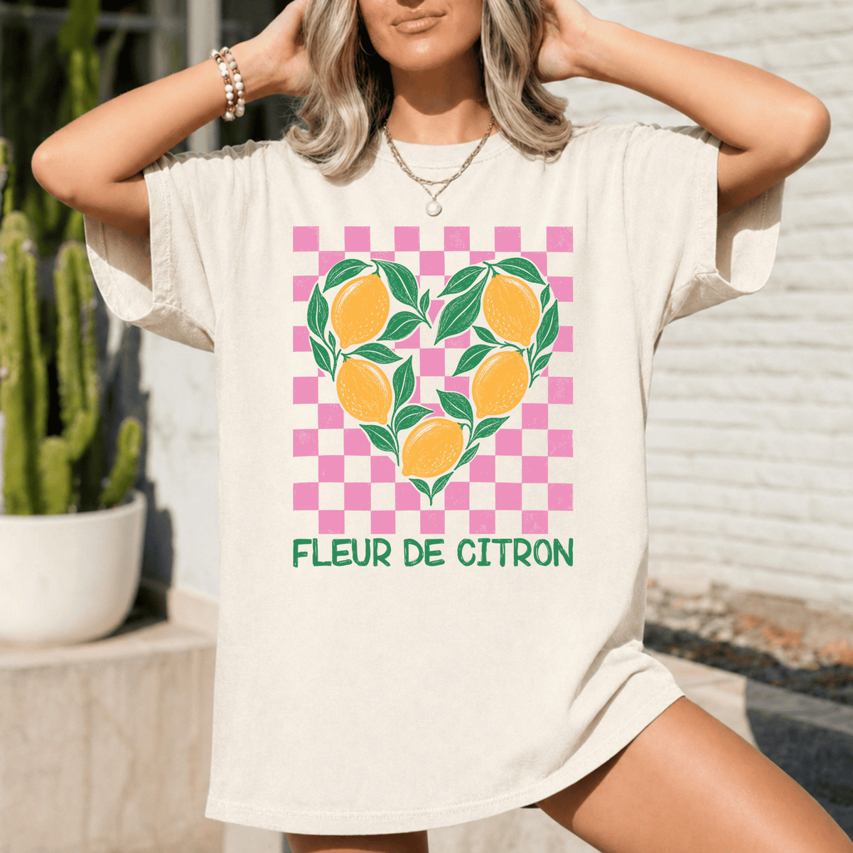 A woman wearing a white t-shirt with a heart-shaped graphic of lemons and green leaves, along with the text "Fleur de Citron" printed on it.