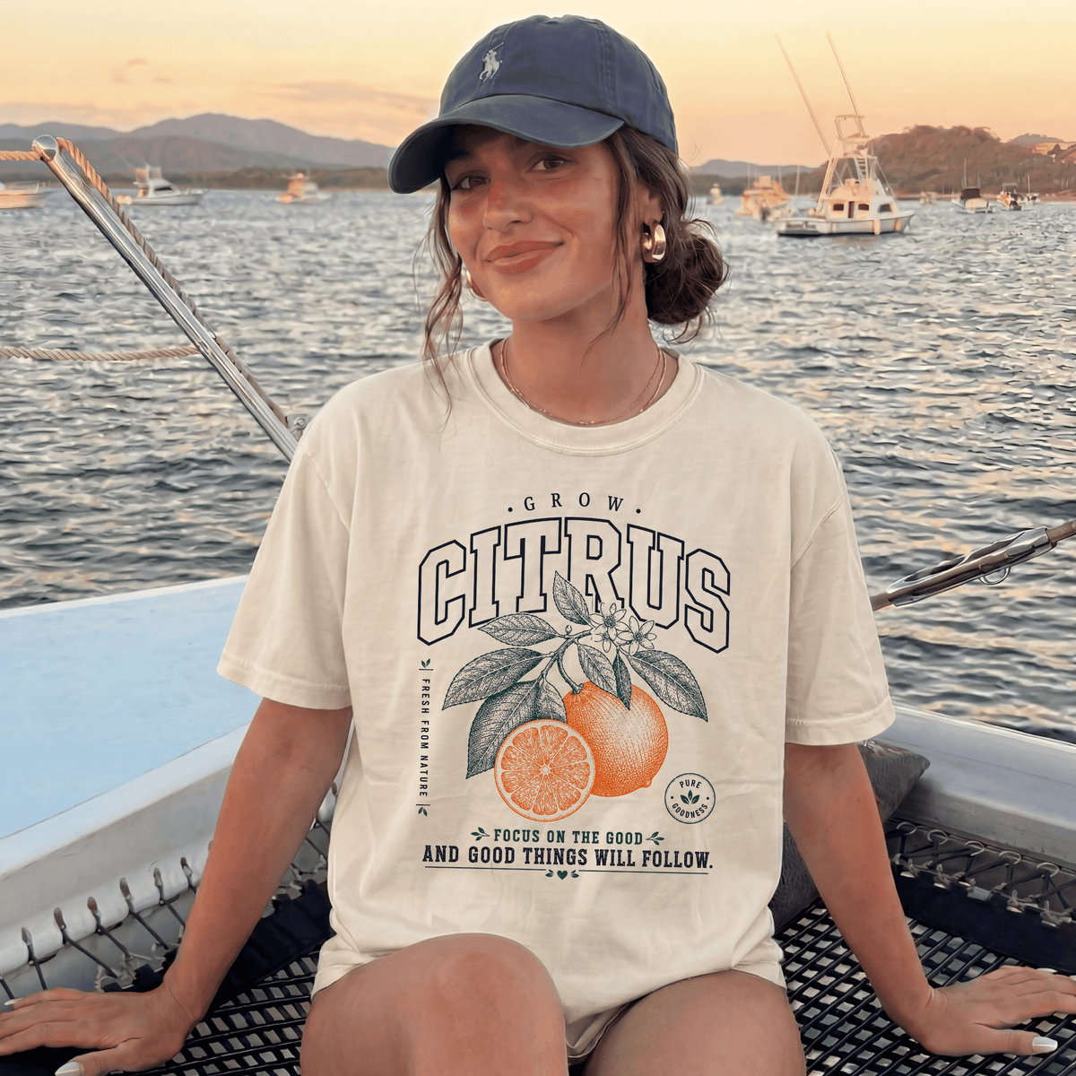 A woman wearing a white t-shirt with a graphic of an orange and text that says "CITRUS" is sitting on a boat in the water.