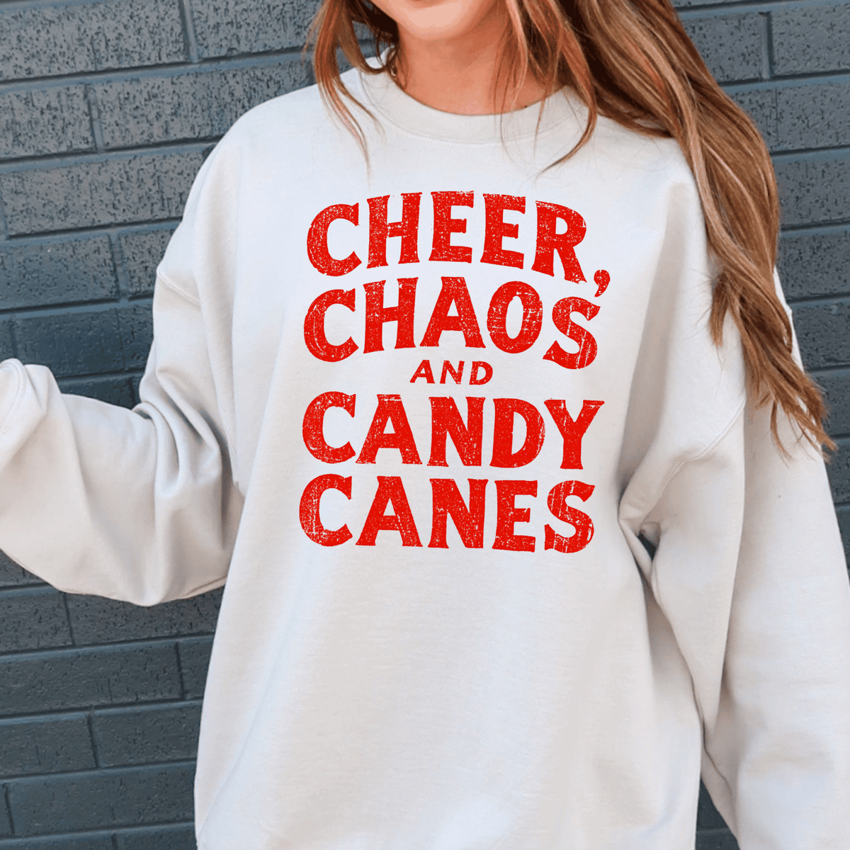 A white sweatshirt with red text that says "CHEER, CHAOS, AND CANDY CANES".