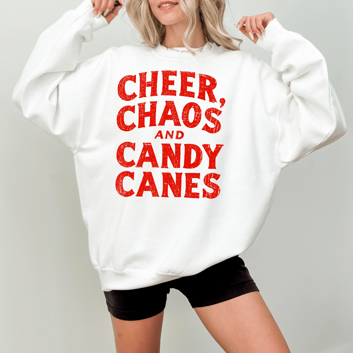 A woman wearing a white sweatshirt with the text "CHEER, CHAOS, AND CANDY CANES" printed on it.