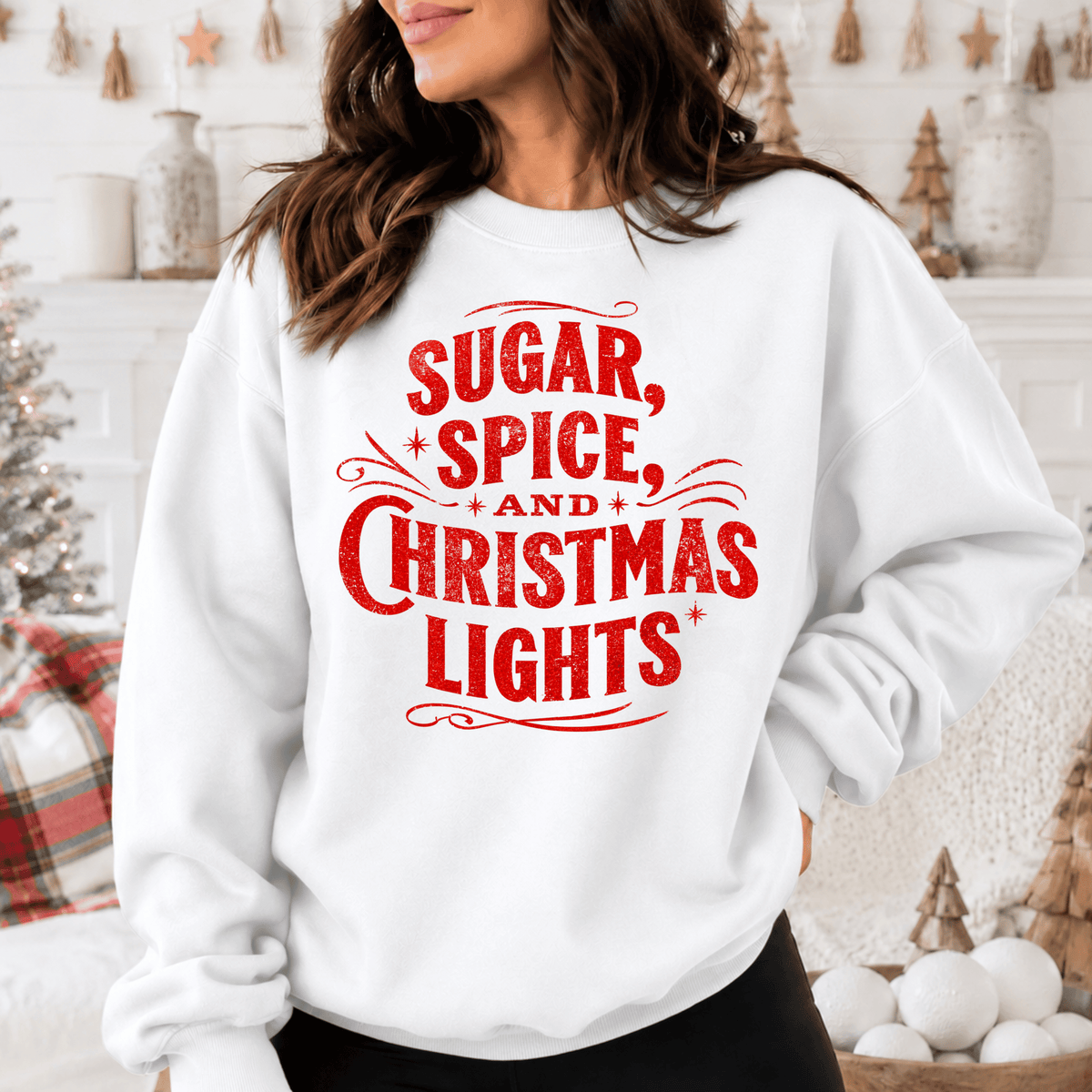 A woman wearing a white sweatshirt with the text "SUGAR, SPICE, AND CHRISTMAS LIGHTS" printed on it.