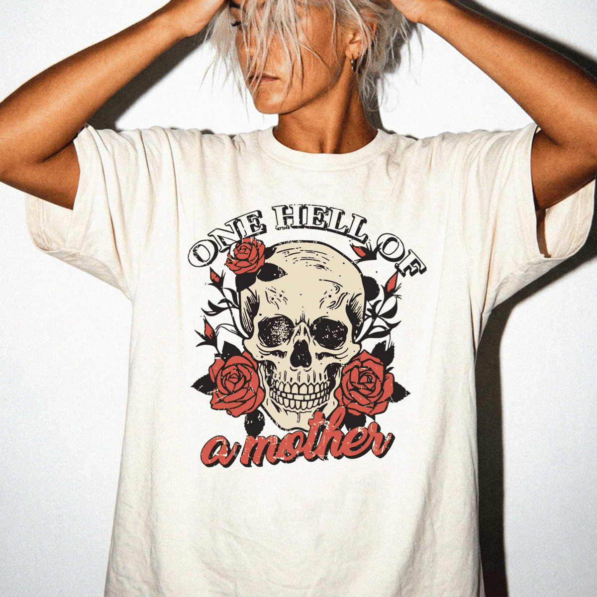 A person wearing a white t-shirt with a skull design and the text "One Hell of a Mother" printed on it.