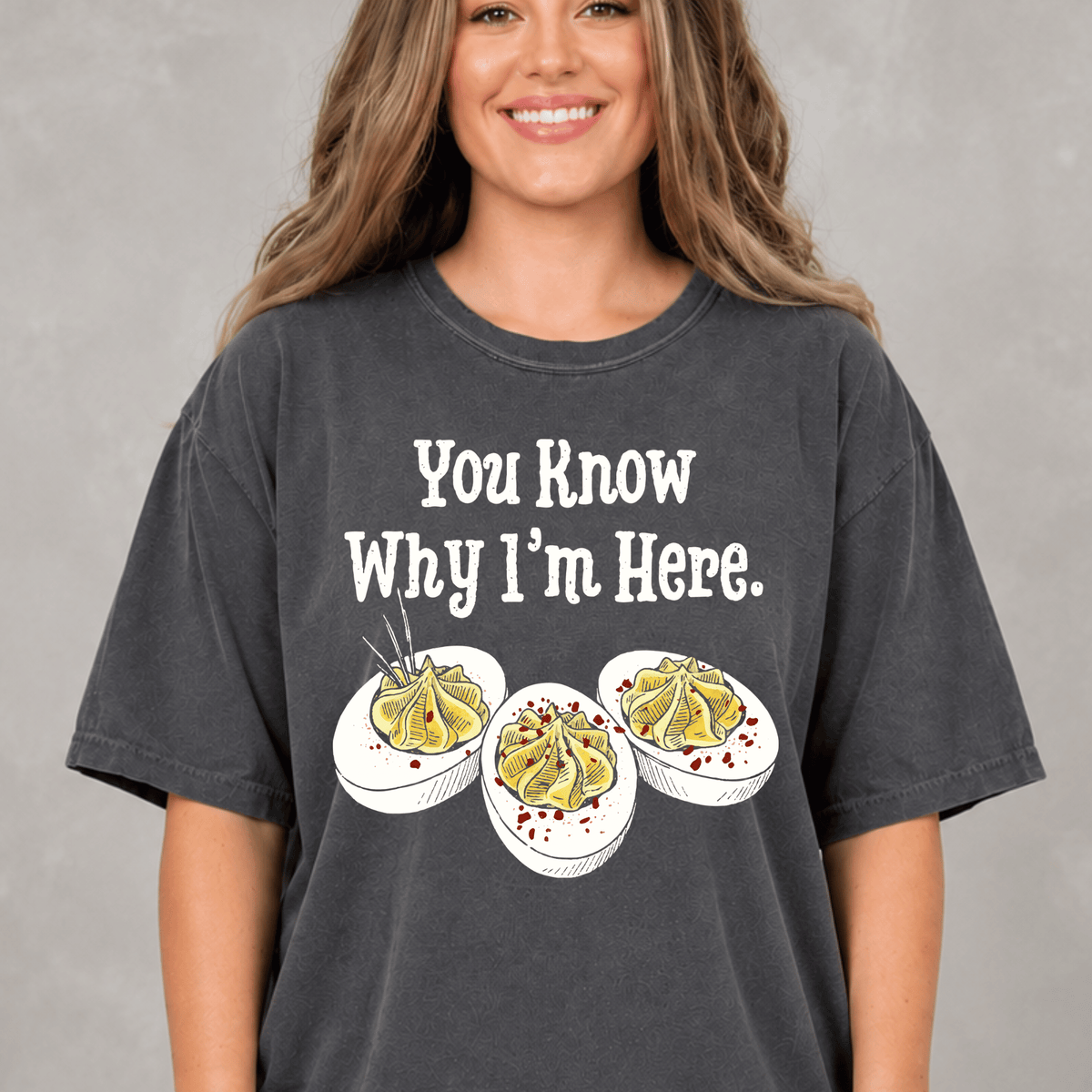 A woman wearing a gray t-shirt with a humorous text and illustrations of food.