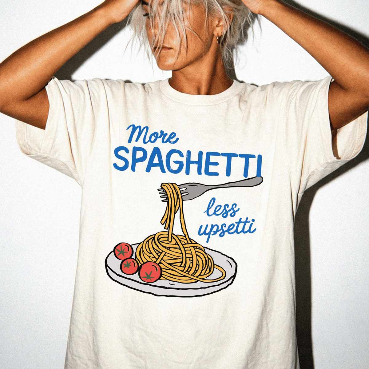 A person wearing a white t-shirt with a graphic design of spaghetti and tomatoes, along with the text "More Spaghetti less Upseti".