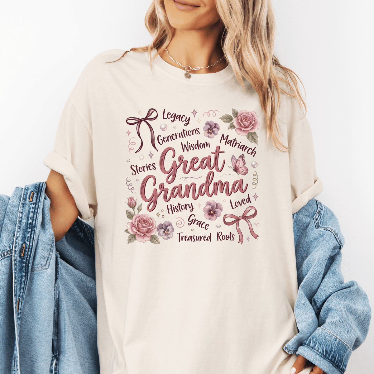 A woman wearing a white t-shirt with a graphic design that says "Great Grandma" surrounded by various words such as "Legacy", " Generations", " Wisdom", "Matriarch", " Stories", "History", "Grace", " Treasured Roots", and "Loved".