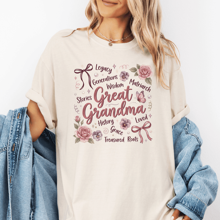 A woman wearing a white t-shirt with a graphic design that says "Great Grandma" surrounded by various words such as "Legacy", " Generations", " Wisdom", "Matriarch", " Stories", "History", "Grace", " Treasured Roots", and "Loved".