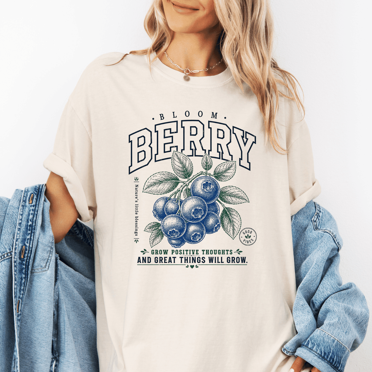 A woman wearing a white t-shirt with a graphic design of blueberries and the text "Bloom Berry" and "Grow positive thoughts and great things will grow".