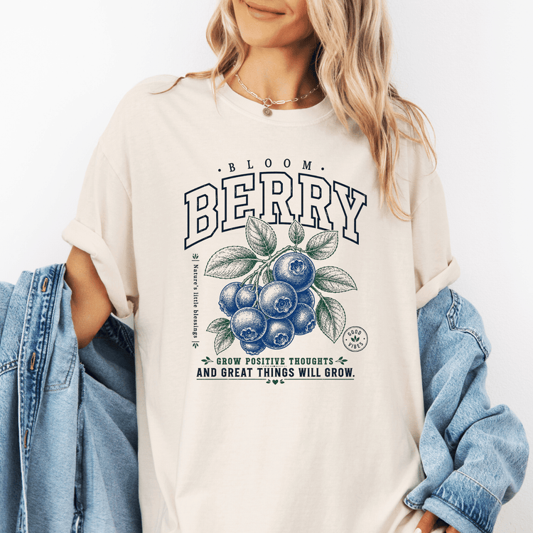 A woman wearing a white t-shirt with a graphic design of blueberries and the text "Bloom Berry" and "Grow positive thoughts and great things will grow".