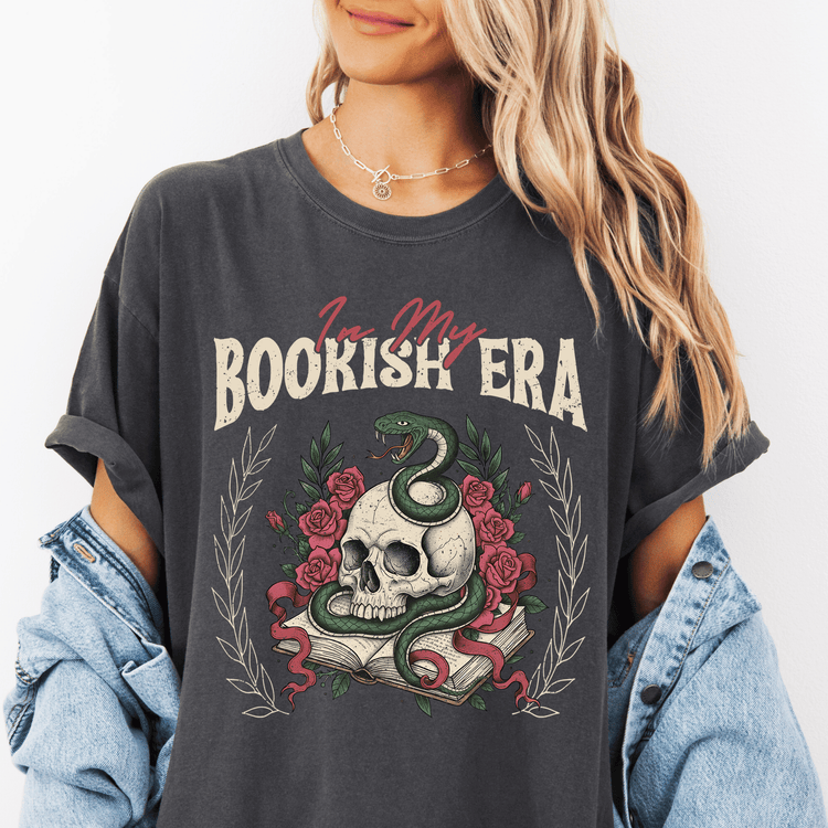 A woman wearing a black t-shirt with a graphic design featuring a skull, a snake, and roses, along with the text "I'm my BOOKISH ERA".