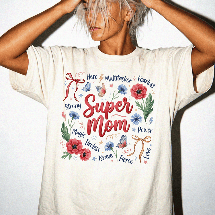 A woman wearing a white t-shirt with a graphic design featuring the words "Super Mom" surrounded by various flowers and butterflies.