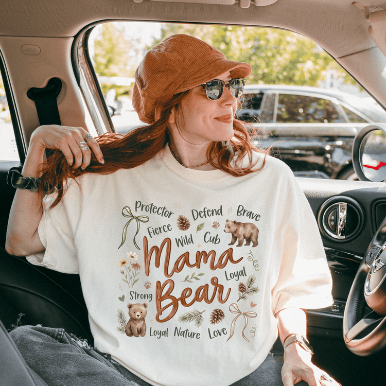 A woman wearing a white t-shirt with a design of a bear and the words "Mama Bear" is sitting in a car.