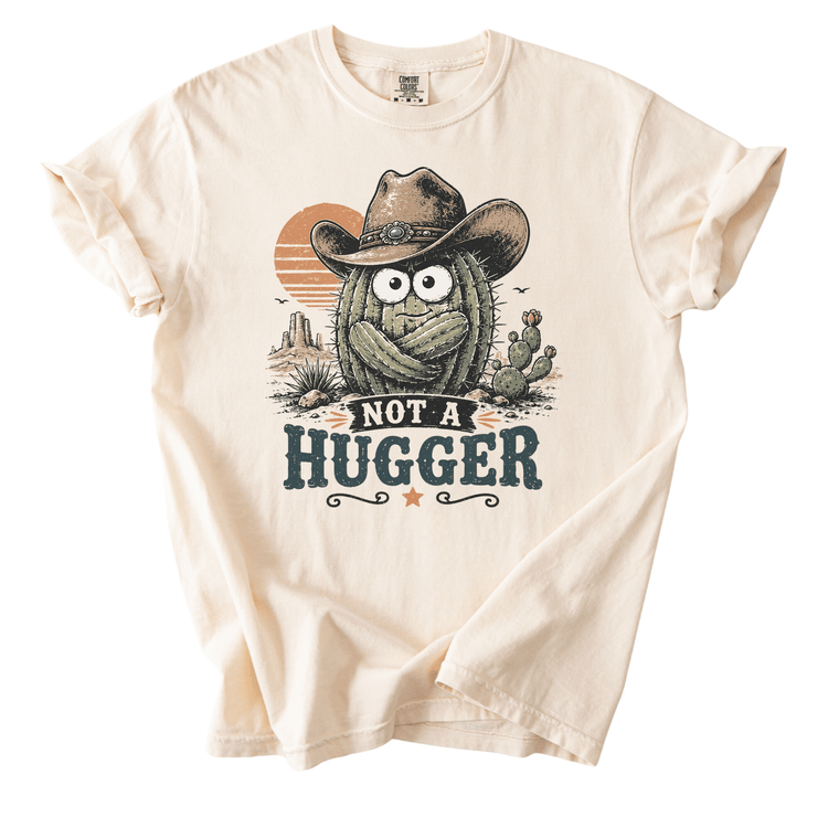 A t-shirt with a graphic design featuring a cactus wearing a cowboy hat and the text "NOT A HUGGER" against a desert landscape background.