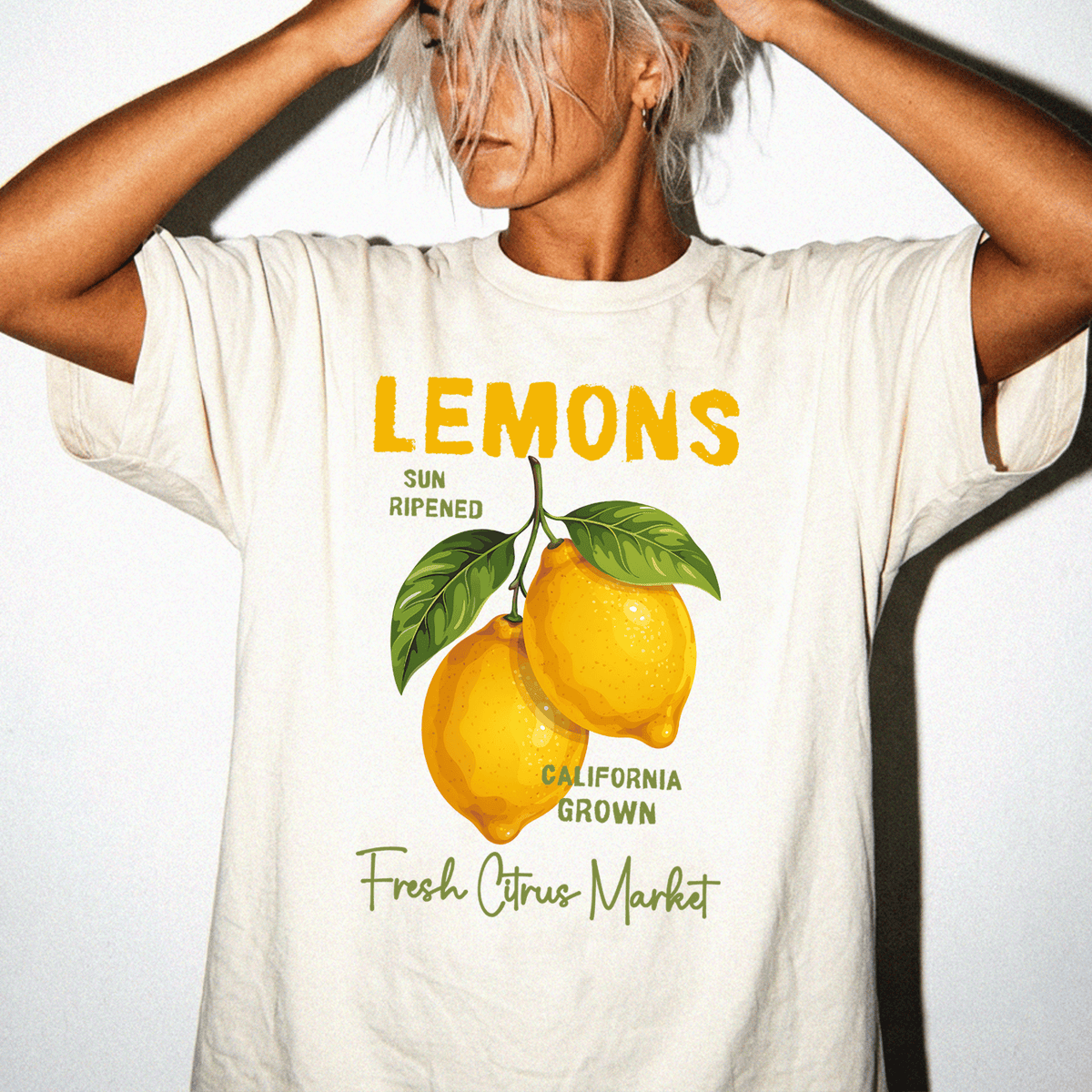 A person wearing a white t-shirt with a graphic design of two lemons and text that reads "LEMONS" and "SUN RIPPENED CALIFORNIA GROWN Fresh Citrus Market".
