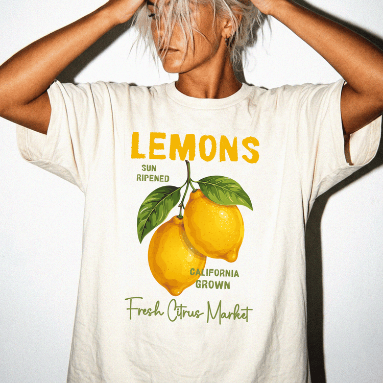 A person wearing a white t-shirt with a graphic design of two lemons and text that reads "LEMONS" and "SUN RIPPENED CALIFORNIA GROWN Fresh Citrus Market".