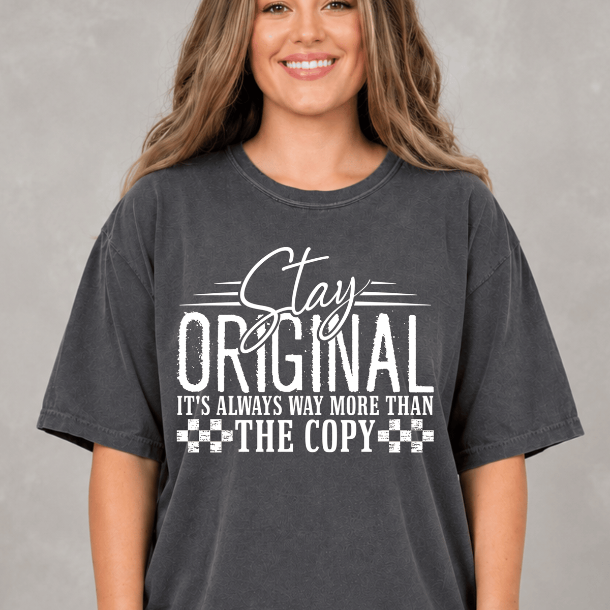 A woman wearing a gray t-shirt with a white text design that says "Stay Original It's Always Way More Than The Copy".