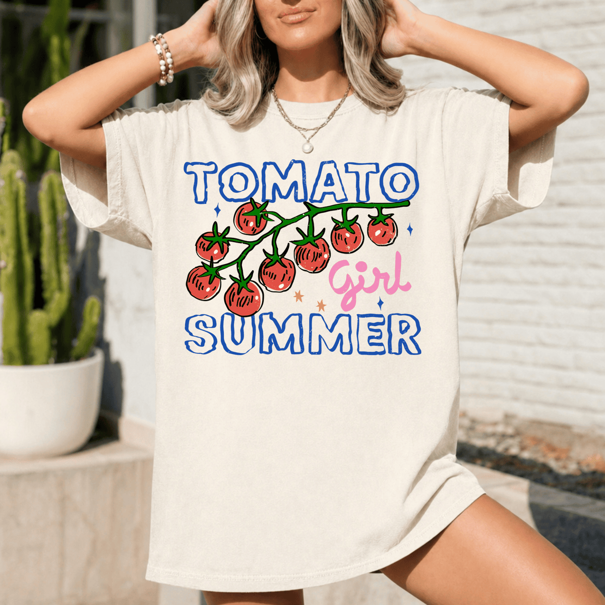A woman wearing a white t-shirt with a graphic design featuring a tomato and the text "Tomato Girl Summer" printed on it.